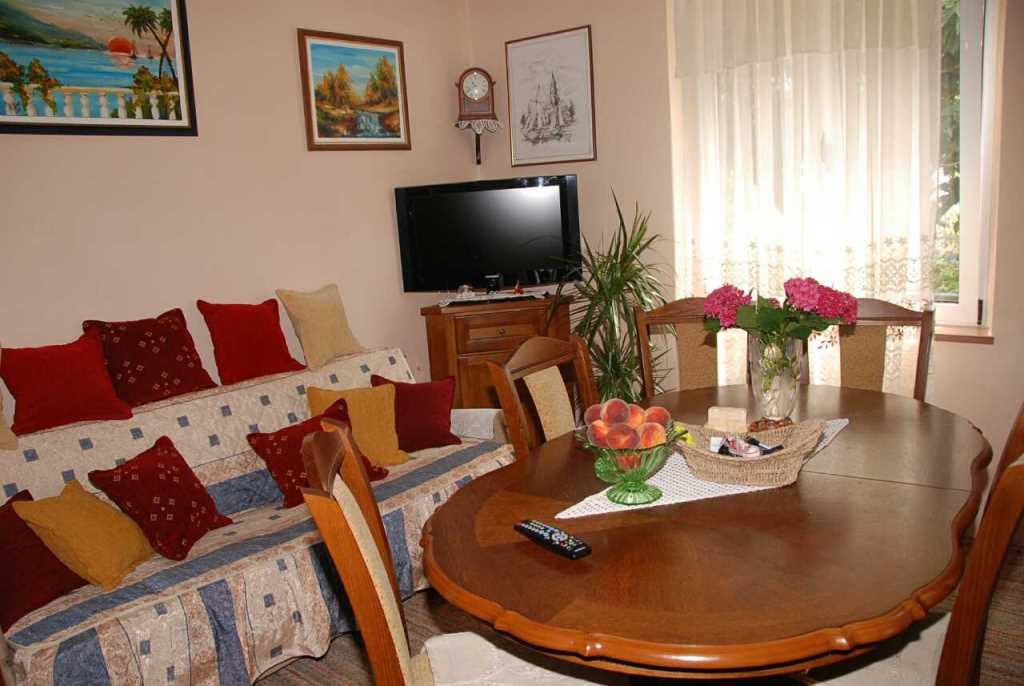 Gemütliches Wohnzimmer in einem Haus in Kamenari, Montenegro: Holzesstisch, weiches Sofa mit Kissen und TV-Bereich.