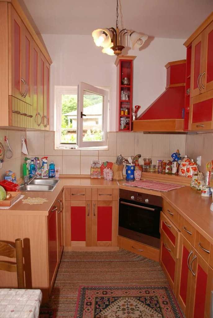 Gemütliche Küche mit roten Fronten in einem Haus in Kamenari, Montenegro: Einbaugeräte, Spüle und Blick aus dem Fenster.