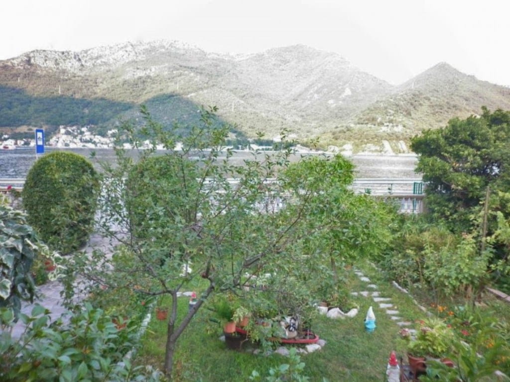 Grüner Garten mit Blick auf das Meer und die Berge am Haus in Kamenari, Montenegro: gepflegtes Grundstück mit Bäumen und Wegen.