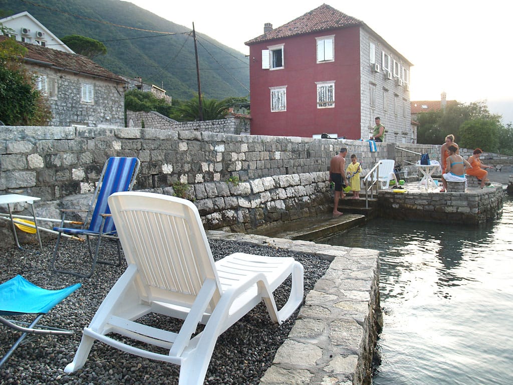 Privatna plaža sa ležaljkama uz kamenu vilu u Stolivu, Crna Gora: pogled na more i tradicionalnu arhitekturu.