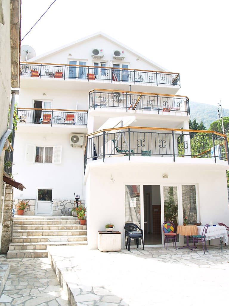 Trospratna bela vila u Stolivu, Crna Gora, sa terasama, baštenskim nameštajem i kamenim detaljima fasade.
