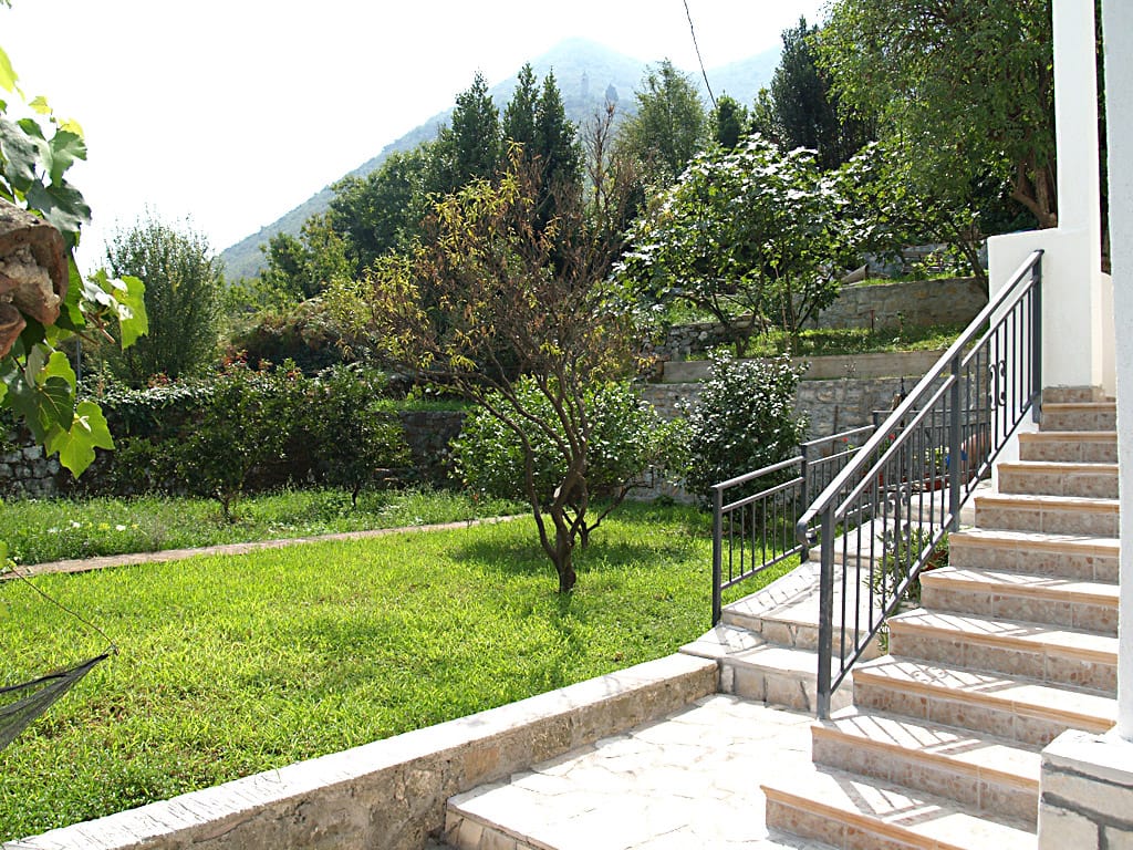 Zelena bašta sa terasom i kamenim stepenicama uz vilu u Stolivu, Crna Gora, sa slikovitim pogledom na planinski pejzaž.