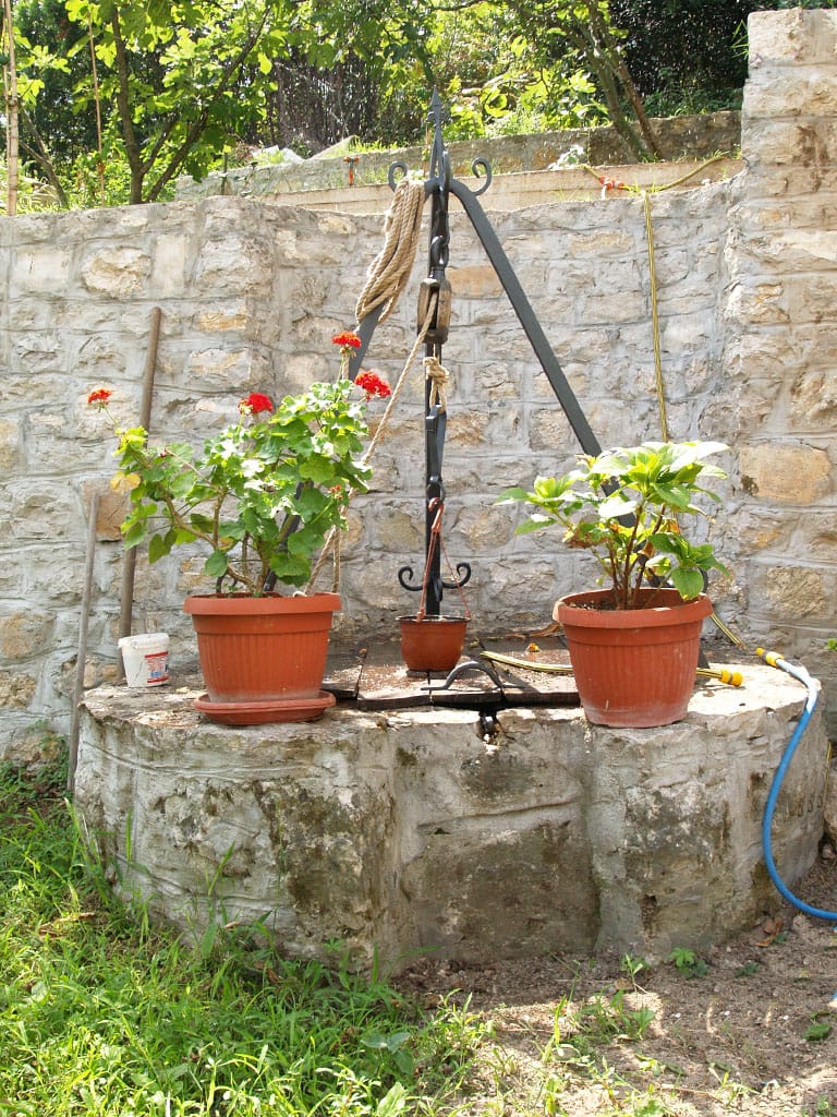 Stari kameni bunar sa cvećem u vrtu vile u Stolivu, Crna Gora: pejzažni dizajn i dekor dvorišta.