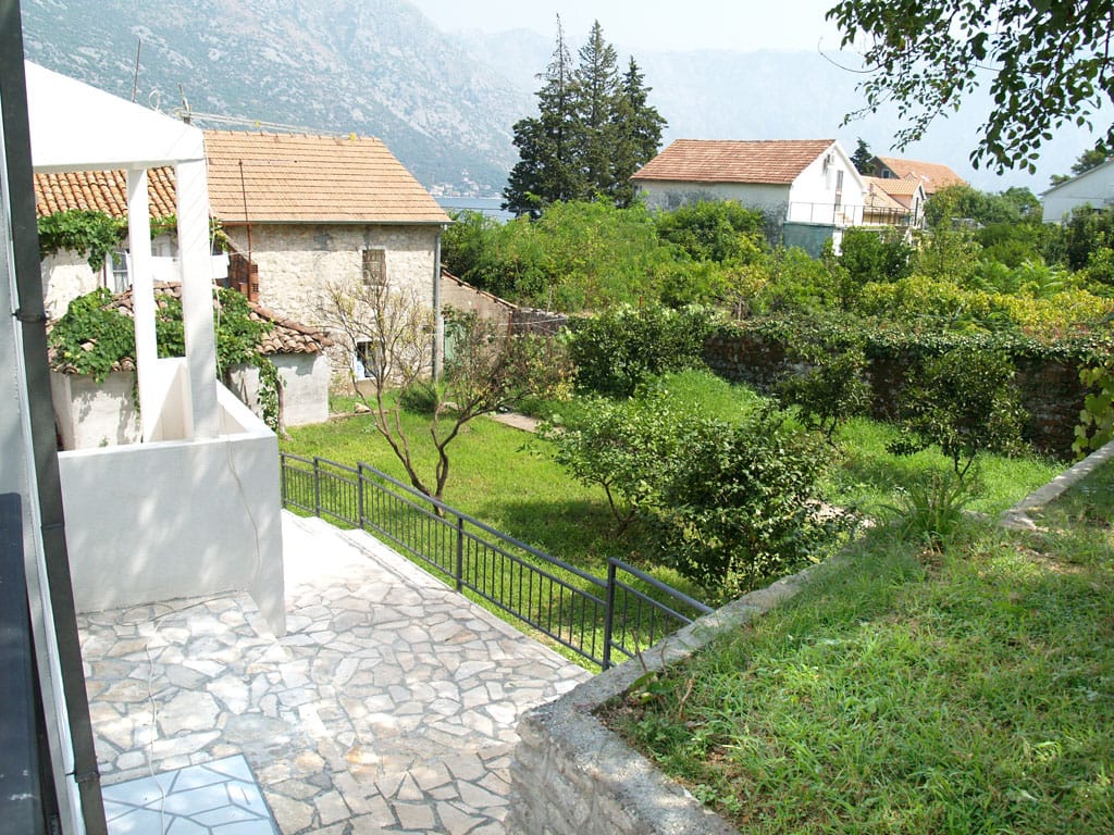 Pogled na zelenu baštu i kamene kuće u Stolivu, Crna Gora, sa terase vile sa kamenim oblogama i planinskim pejzažom.