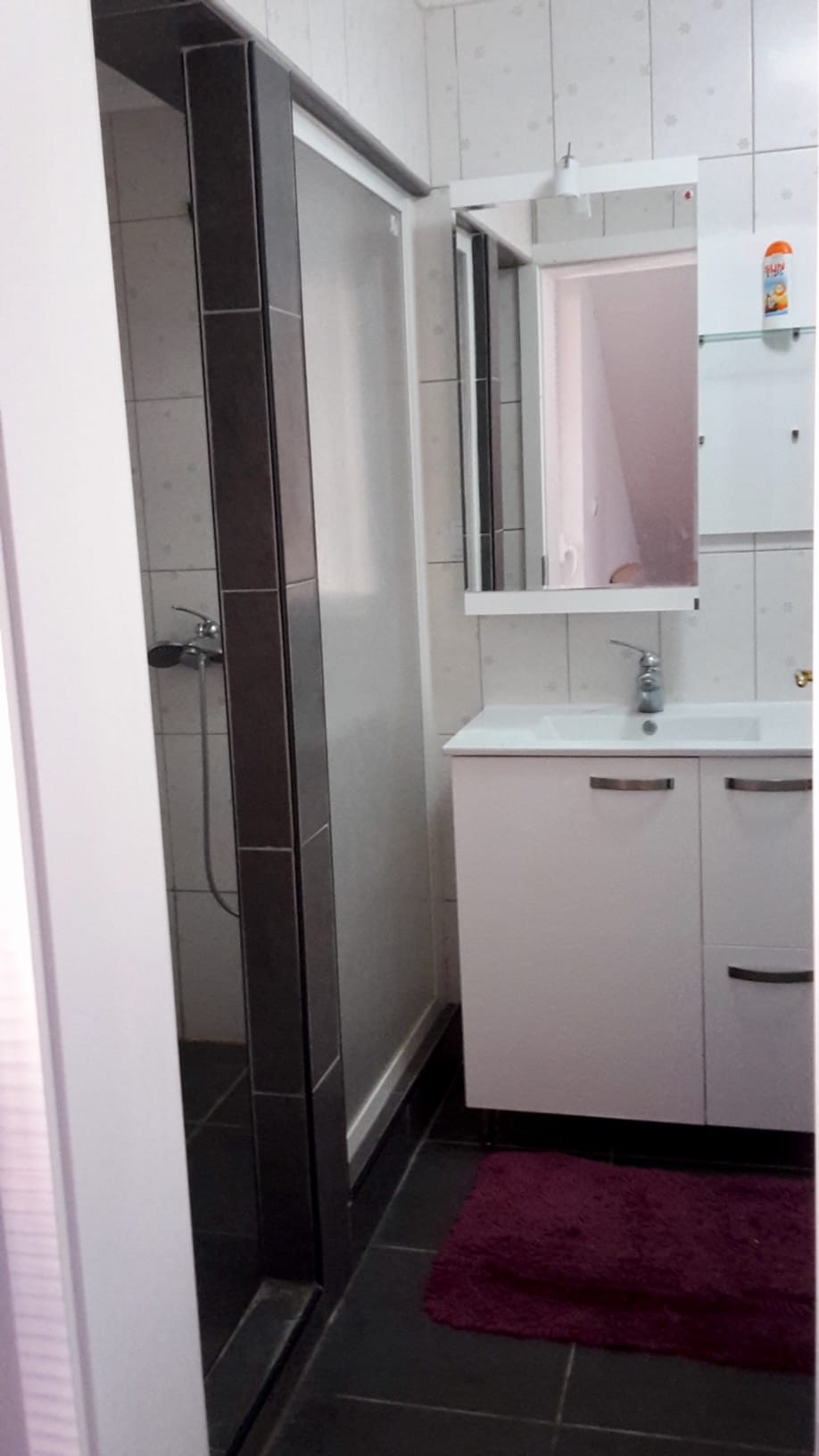 Badezimmer in der Wohnung, Đenovići, Montenegro: weiße Waschtischkonsole mit Waschbecken, Spiegel und Duschkabine mit dunklen Fliesen.