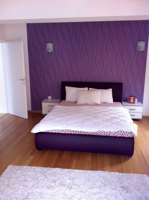 Schlafzimmer in einer Wohnung in Đenovići, Montenegro: Doppelbett, violette Tapete mit Muster und Parkettboden.
