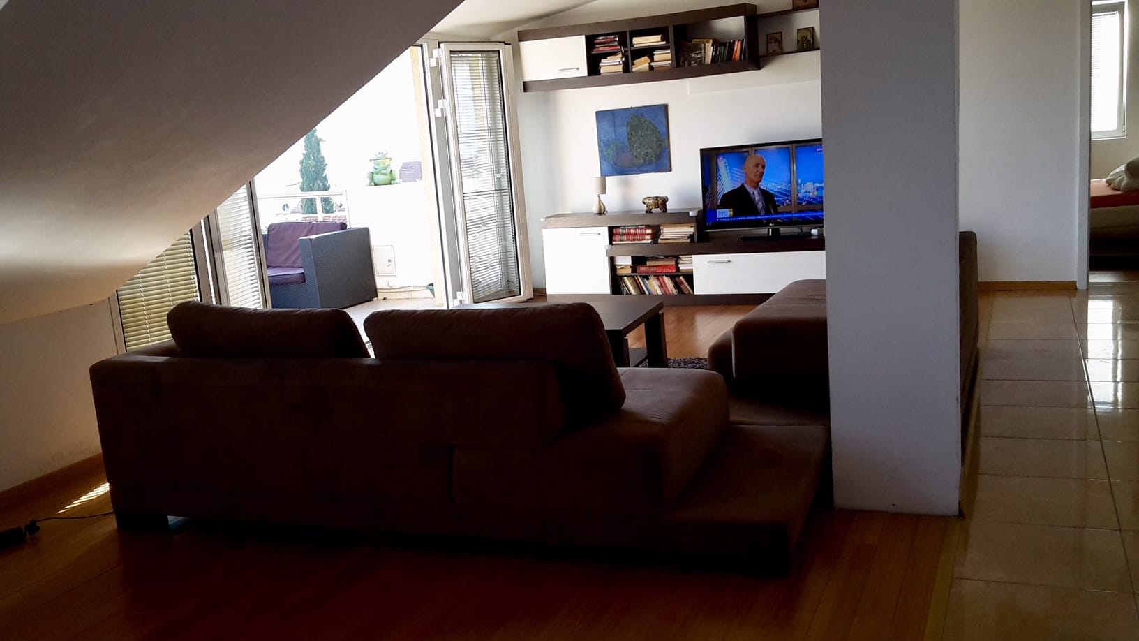 Wohnzimmer in einer Dachgeschosswohnung in Đenovići, Montenegro: weiches Sofa, TV-Bereich, Zugang zur Terrasse und Parkettboden.