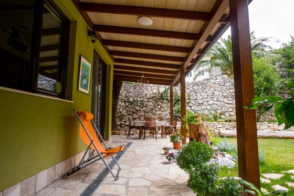 Gemütliche Terrasse eines Hauses in Orahovac, Montenegro: Steinmauerwerk, Holzüberdachung, Möbel und Blick auf den grünen Garten.