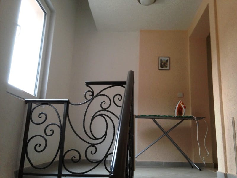 Stepenište sa kovanom ogradom i daska za peglanje u kući, grad Dobri Vodi, Crna Gora. Svetao enterijer sa prozorom.