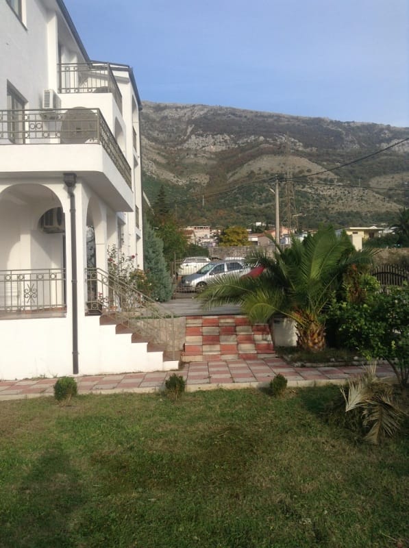 Bela kuća sa terasama, baštom i pogledom na planine u Sutomoru, Crna Gora. Plac sa palmom i parkingom uz kuću.