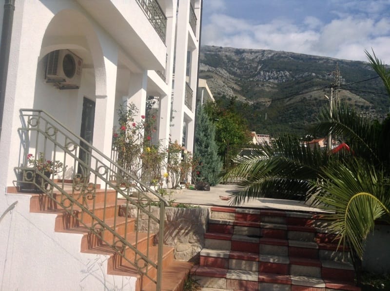 Bela kuća u Sutomoru, Crna Gora: terasa sa kovanim ogradama, palme i slikovit pogled na planine pored smeštaja.
