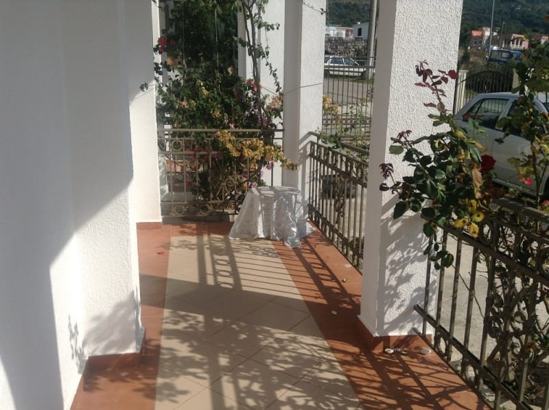 Ugodna terasa sa kovanom ogradom i cvećem u kući u Sutomoru, Crna Gora: pločice na podu i pogled na ulicu.