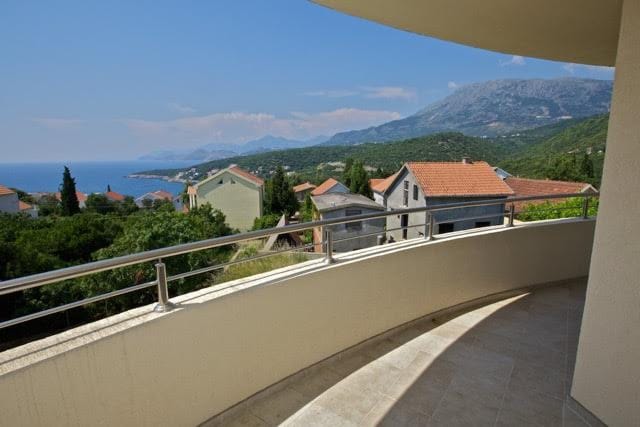 Panoramic view of the sea and mountains from the spacious balcony of a villa in Utjeha, Montenegro, with a stone floor and railing.