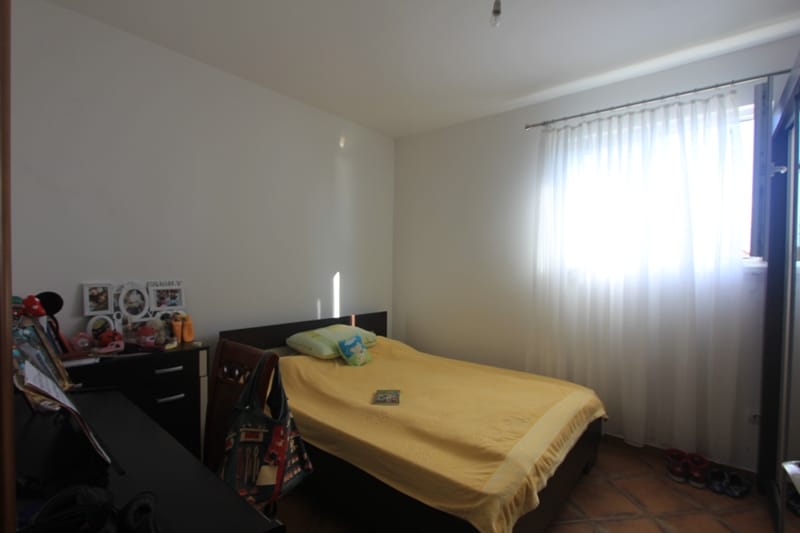 Bright bedroom with a double bed and dark furniture in a house in Shushan, Montenegro. Tiled floor, view of the window.