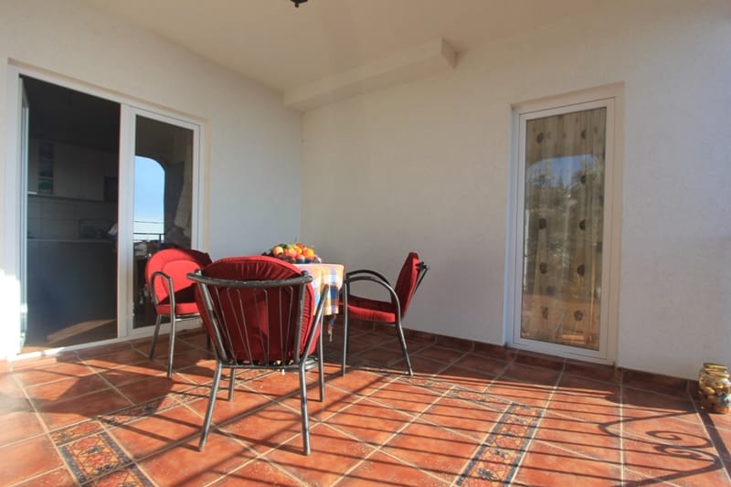 Spacious terrace with red chairs and tiled flooring in a house in Shushan, Montenegro, with access from the kitchen to the balcony.