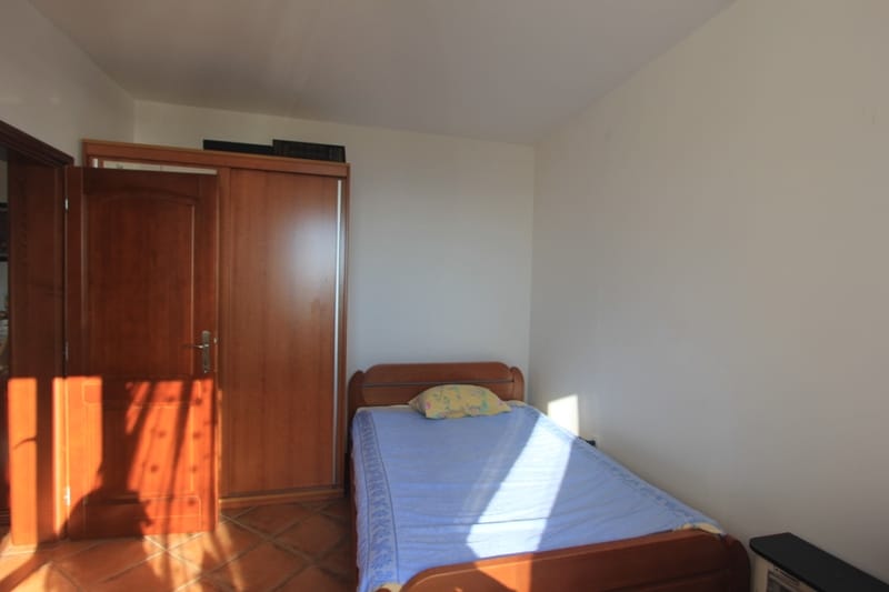 Bedroom with a wooden bed and wardrobe in a house, Shushan, Montenegro. Bright room with tiled floors and furniture.