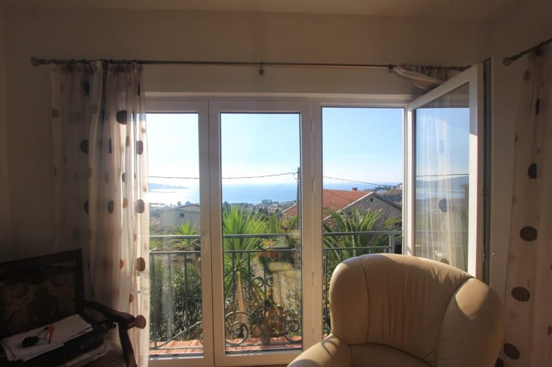Living room with panoramic sea and mountain views in a house in Shushan, Montenegro, with access to the balcony and a leather armchair.