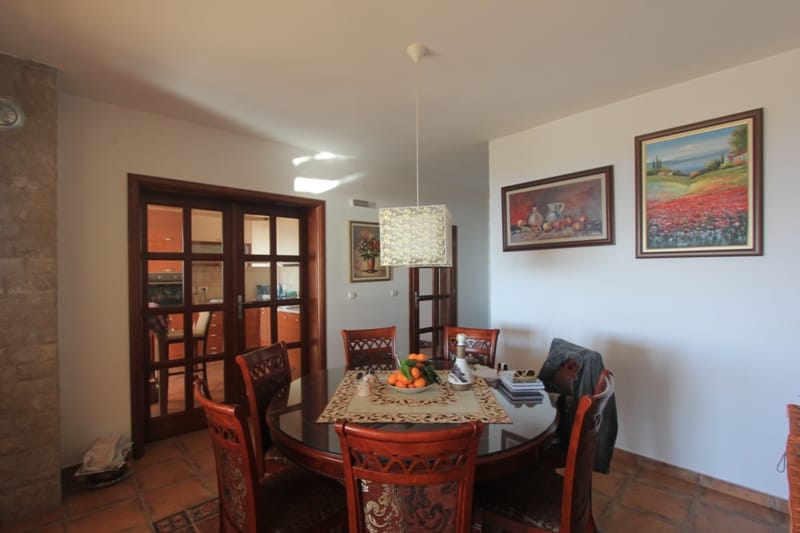 Dining area in a house in Shushan, Montenegro: a round wooden table, upholstered chairs, and a view of the kitchen through the doors.