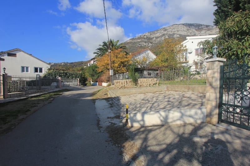 View of a private house and surrounding grounds in Shushan, Montenegro, with a mountain landscape in the background.