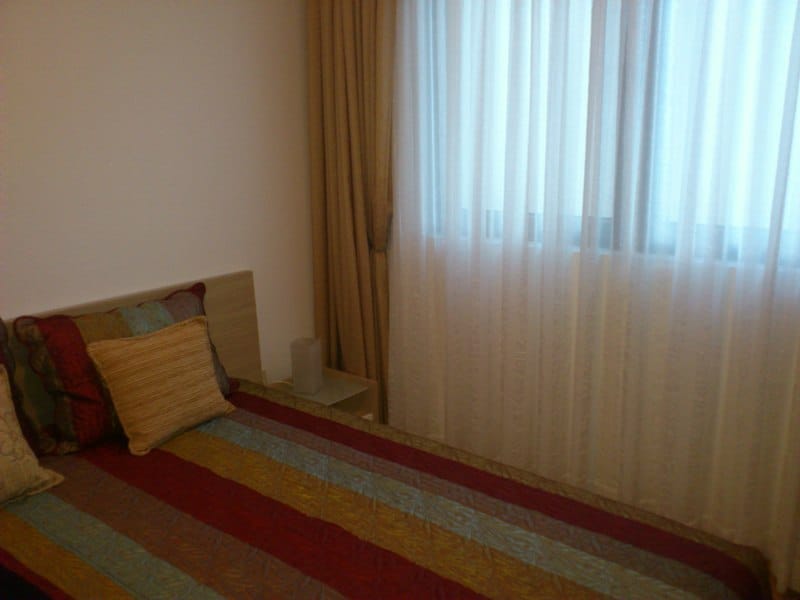 Gemütliches Schlafzimmer mit Doppelbett in einer Wohnung in Pržno, Montenegro: helle Einrichtung und blickdichte Vorhänge an den Fenstern.