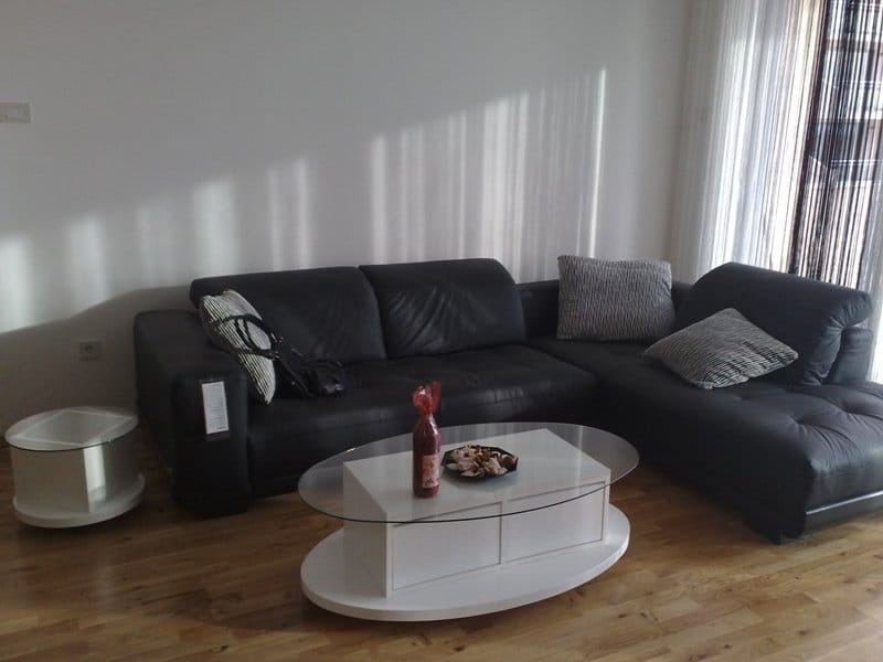 Wohnzimmer in einer Wohnung in Pržno, Montenegro: schwarzes Lederecksofa, weißer ovaler Couchtisch und Parkett.