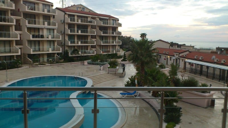Blick vom Balkon auf den Pool und die Wohnanlage in Pržno, Montenegro: moderne Architektur, Palmen und Meereslandschaft.