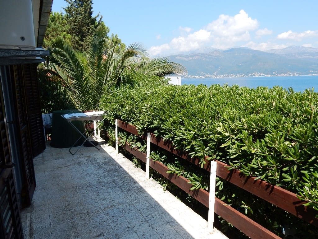 Balkon stana u Krašićima, Crna Gora, s pogledom na more, planine i živom ogradom duž drvene ograde.