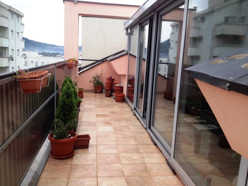 Prostran balkon sa terakota pločicama i biljkama u stanu u gradu Bar, Crna Gora, panoramsko zastakljivanje.
