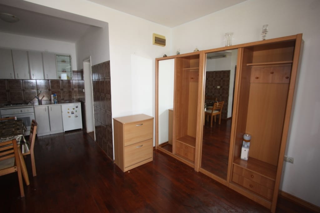 Dnevna soba sa drvenim ormarom i kuhinjskim delom u kući na Luštici, Crna Gora: enterijer sa drvenim podom i nameštajem.