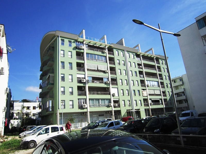 Savremena višespratna stambena zgrada sa balkonima u gradu Bar, Crna Gora, pogled na fasadu i parking ispred zgrade.