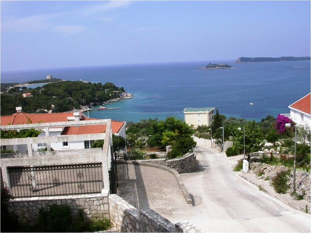 Panoramski pogled na more i obalu Luštice, Crna Gora: kuća sa terasom, prilazni put i zeleni pejzaž.
