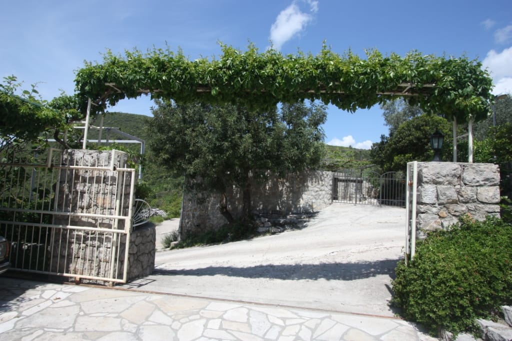 Ulaz na teritoriju kuće u Luštici, Crna Gora: kamena kapija, pergola obrasla zelenilom i popločano dvorište.