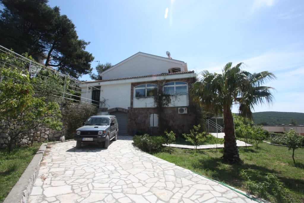 Dvospratna kuća u Luštici, Crna Gora: kamena fasada, parking, palma i bašta na pripadajućem placu.