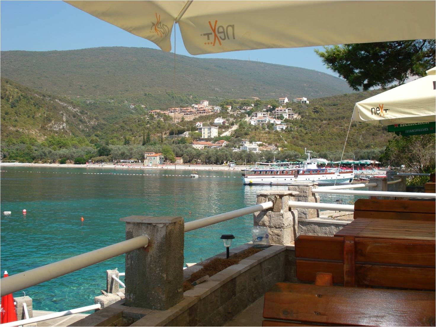 Pogled sa terase kuće u Luštici, Crna Gora: drveni nameštaj, suncobrani i panoramski pogled na more i planine.