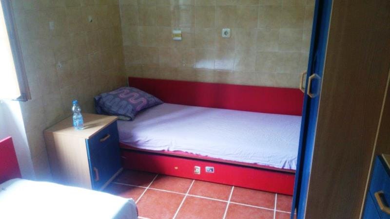 Chambre dans une maison à Dobrota, Monténégro : lit rouge, table de chevet, revêtement en carrelage des murs et du sol, vue de l’intérieur.