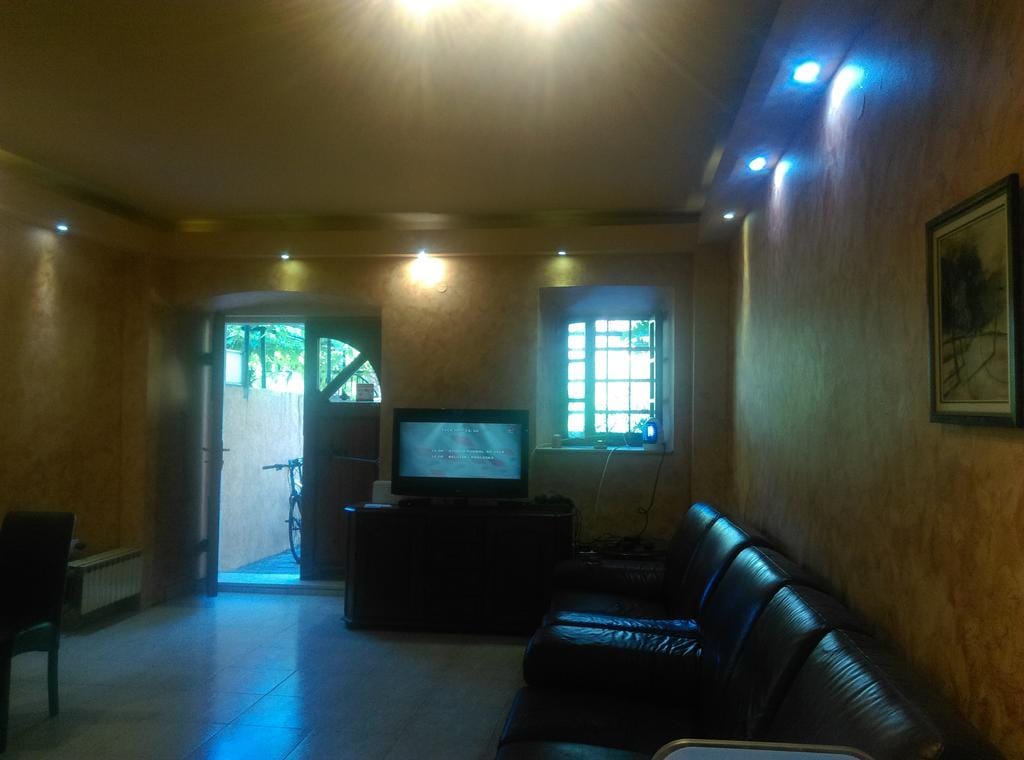 Salon avec canapé en cuir et TV dans une maison à Dobrota, Monténégro : intérieur chaleureux avec éclairage ponctuel et accès à la cour.