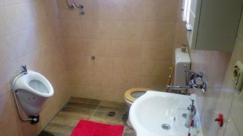 Salle de bains dans une maison à Dobrota, Monténégro : carrelage clair, lavabo, toilettes et urinoir, sanitaires de qualité.