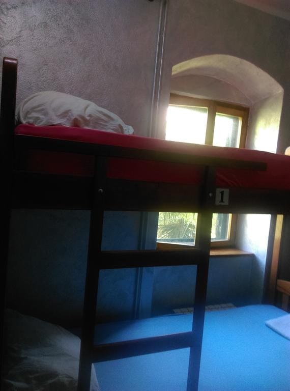 Lit superposé dans la chambre d’une maison à Dobrota, Monténégro : pièce lumineuse avec fenêtre cintrée et mobilier en bois.