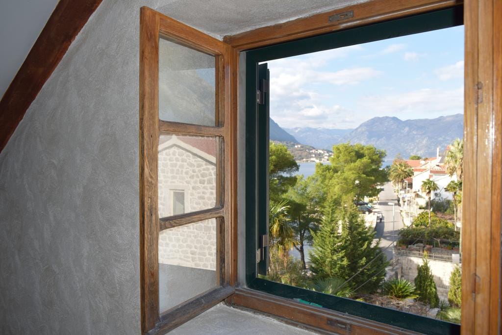 Vue depuis la fenêtre en bois du grenier sur la mer et les montagnes dans une maison, ville de Dobrota, Monténégro. Finition murale grise, vue panoramique.