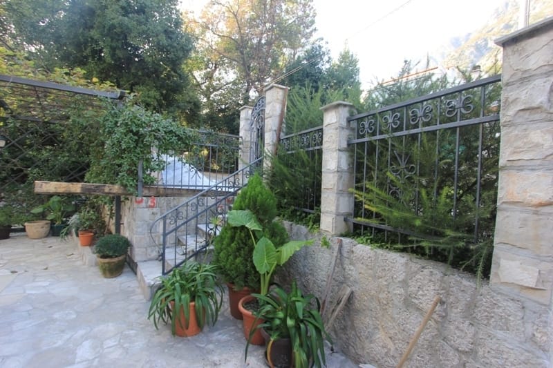 Cour intérieure chaleureuse avec finition en pierre, clôture en fer forgé et plantes vertes près de la maison à Dobrota, Monténégro.