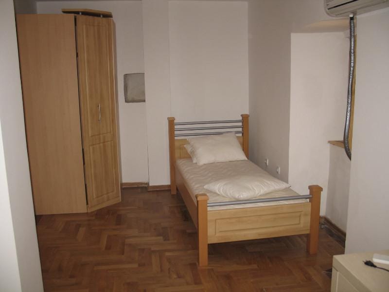 Chambre avec un lit simple et une armoire dans une maison, ville de Dobrota, Monténégro : pièce lumineuse avec parquet.