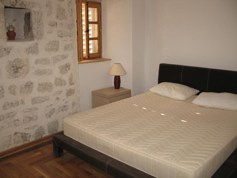 Chambre dans une maison en pierre à Dobrota, Monténégro : lit double, mur en pierre authentique et fenêtre en bois.