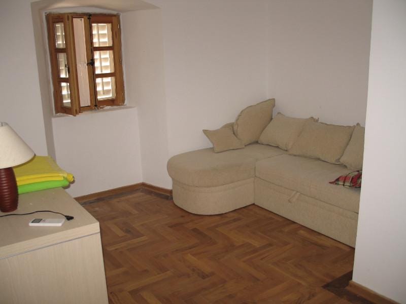 Salon avec canapé d’angle beige et parquet dans une maison à Dobrota, Monténégro. Volets en bois à la fenêtre.