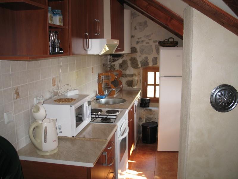 Cuisine sous les combles d’une maison à Dobrota, Monténégro : façades en bois, murs en pierre, électroménager intégré et carrelage.