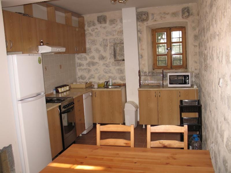 Cuisine dans une maison en pierre à Dobrota, Monténégro : mobilier en bois, appareils électroménagers et murs en pierre authentiques.