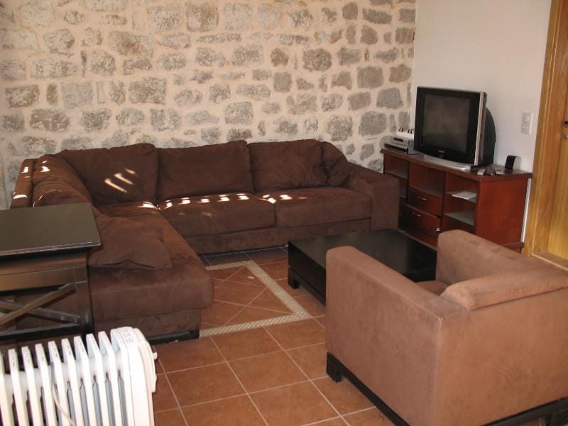 Salon dans une maison à Dobrota, Monténégro : canapé marron moelleux, mur en pierre apparente et sol carrelé.