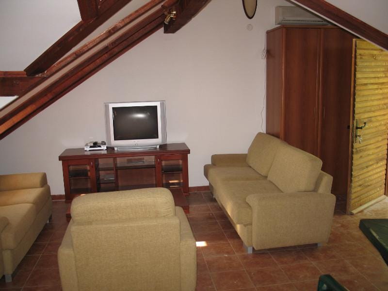 Salon sous les combles d’une maison à Dobrota, Monténégro : mobilier moelleux, poutres en bois, meuble TV et sol carrelé.