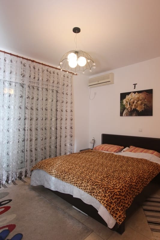 Spavaća soba u stanu u Bečićima, Crna Gora: bračni krevet, klima-uređaj, panoramski prozori sa tilom i stilizovan dekor.