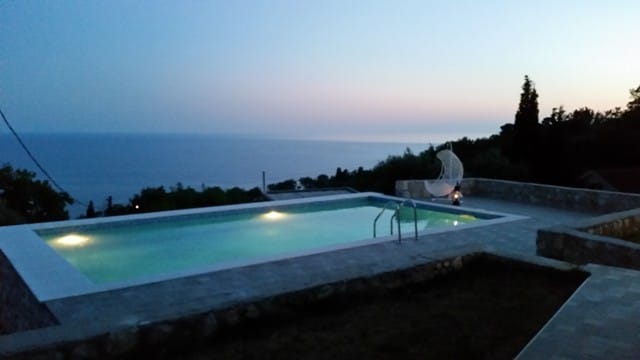 Outdoor pool with lighting and sea view at a villa in Shushan, Montenegro, with a lounge area and a cocoon chair.