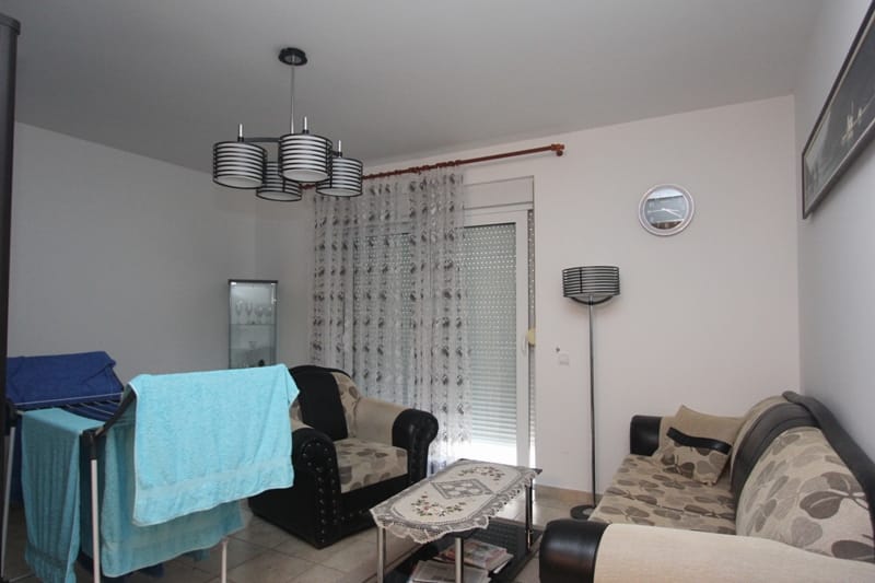 Dnevna soba u stanu u Bečićima, Crna Gora: mekani nameštaj, klub sto, savremeni luster i izlaz na balkon.